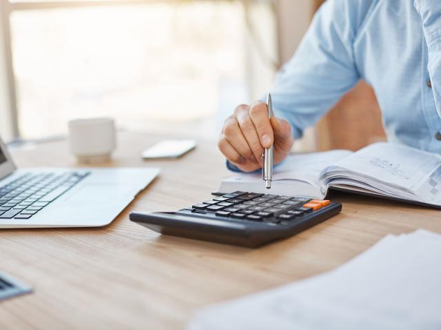 Close up detail of professional serious accountant sitting in light office, checking company finance profits on calculator, writing down results in notebook. Business concept.