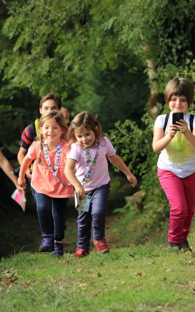 3 enfants et 2 adultes sur un chemin effectuant un parcours Terra Aventura, téléphone en main