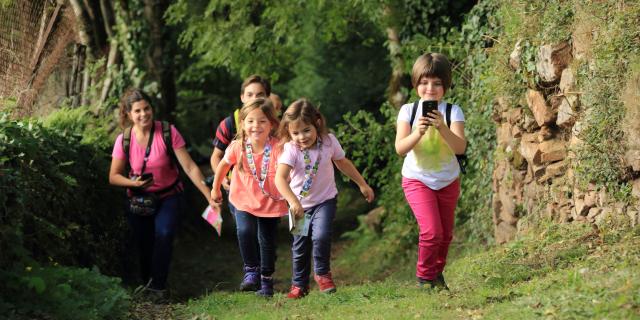 3 enfants et 2 adultes sur un chemin effectuant un parcours Terra Aventura, téléphone en main