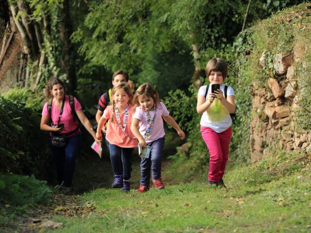 3 enfants et 2 adultes sur un chemin effectuant un parcours Terra Aventura, téléphone en main