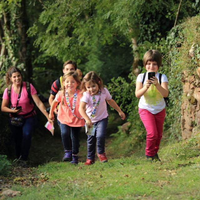 3 enfants et 2 adultes sur un chemin effectuant un parcours Terra Aventura, téléphone en main