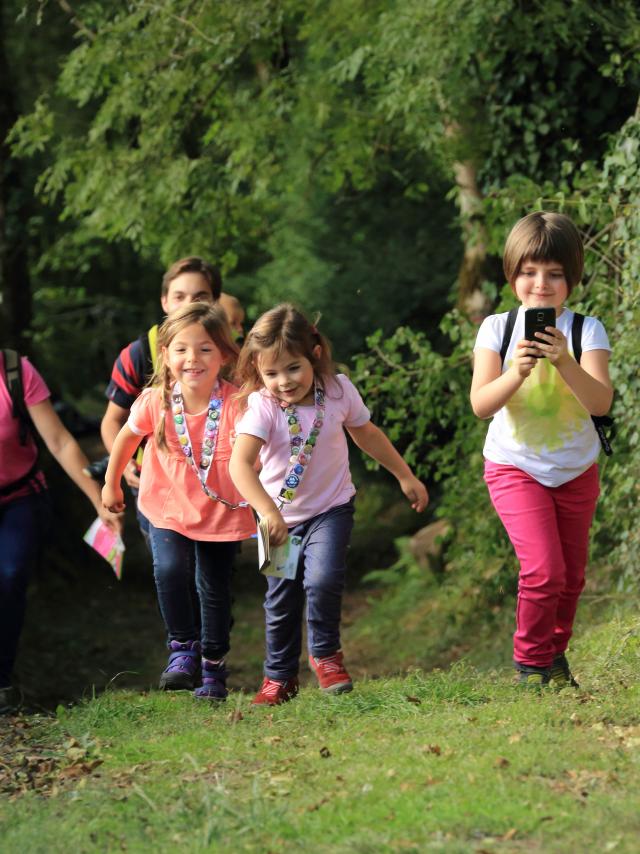 3 enfants et 2 adultes sur un chemin effectuant un parcours Terra Aventura, téléphone en main