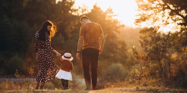 Une famille de 3 personnes qui marchent dans la nature, au soleil couchant