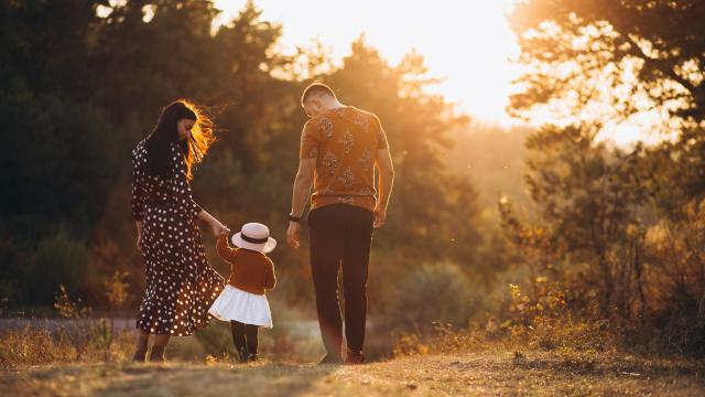 Une famille de 3 personnes qui marchent dans la nature, au soleil couchant