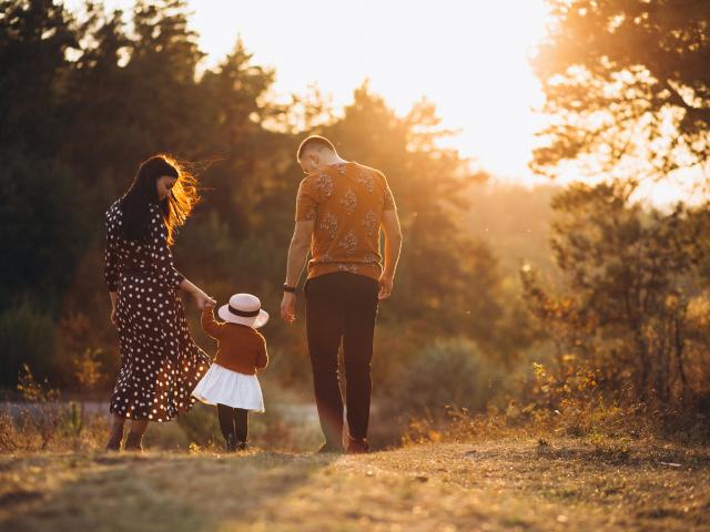 Une famille de 3 personnes qui marchent dans la nature, au soleil couchant