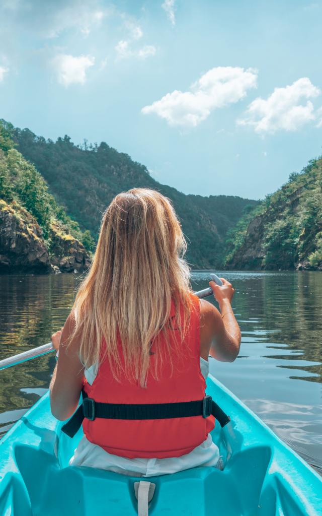 Une femme blonde pagaie sur la Dordogne à bord d'un canoe bleu