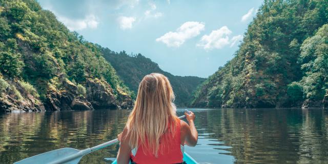 Une femme blonde pagaie sur la Dordogne à bord d'un canoe bleu