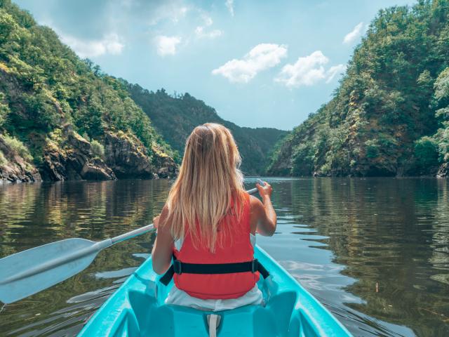 Une femme blonde pagaie sur la Dordogne à bord d'un canoe bleu