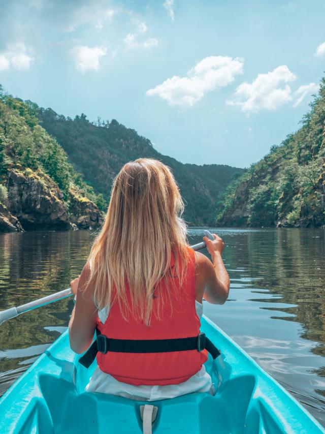 Une femme blonde pagaie sur la Dordogne à bord d'un canoe bleu